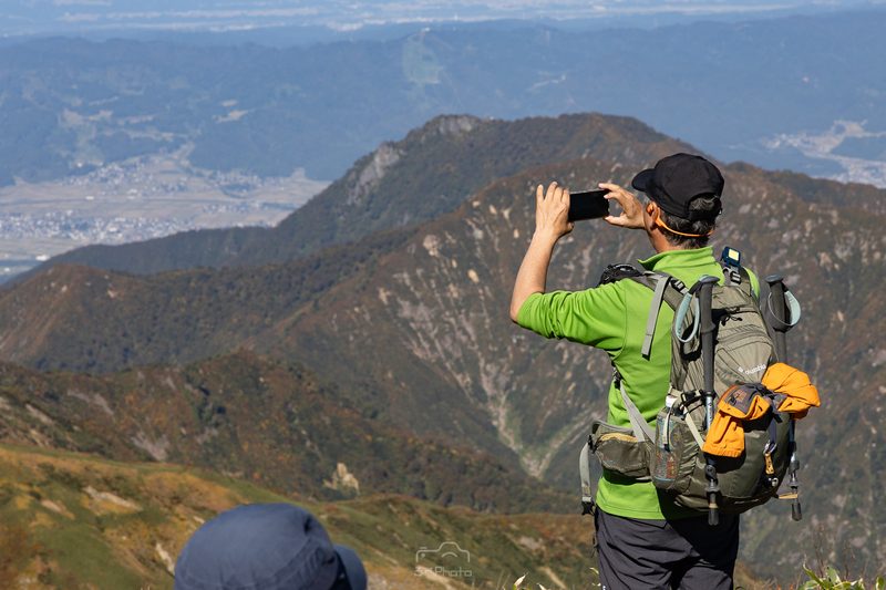 牛ヶ岳展望台から六日町方面を撮影する登山者の写真
